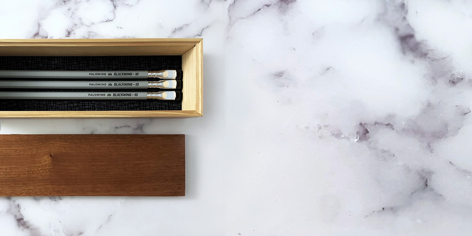 A wooden pencil box with pencils on black and white marble